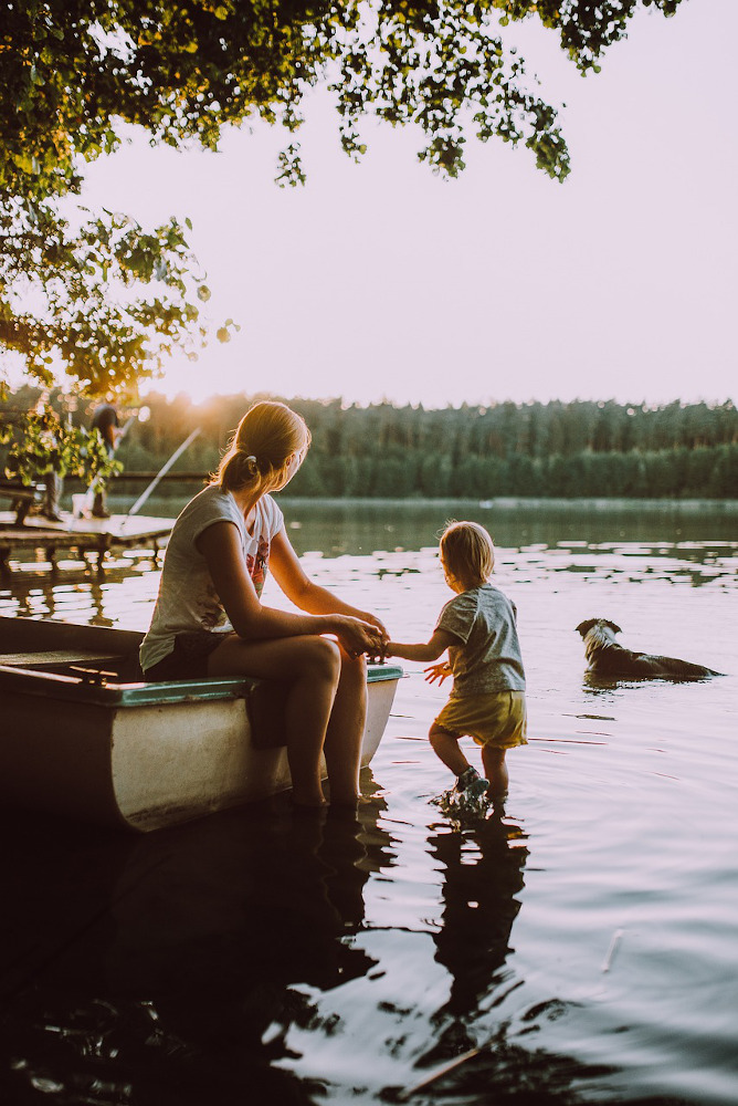 Relaxed scene of woman in boat, feet in water, child paddling.