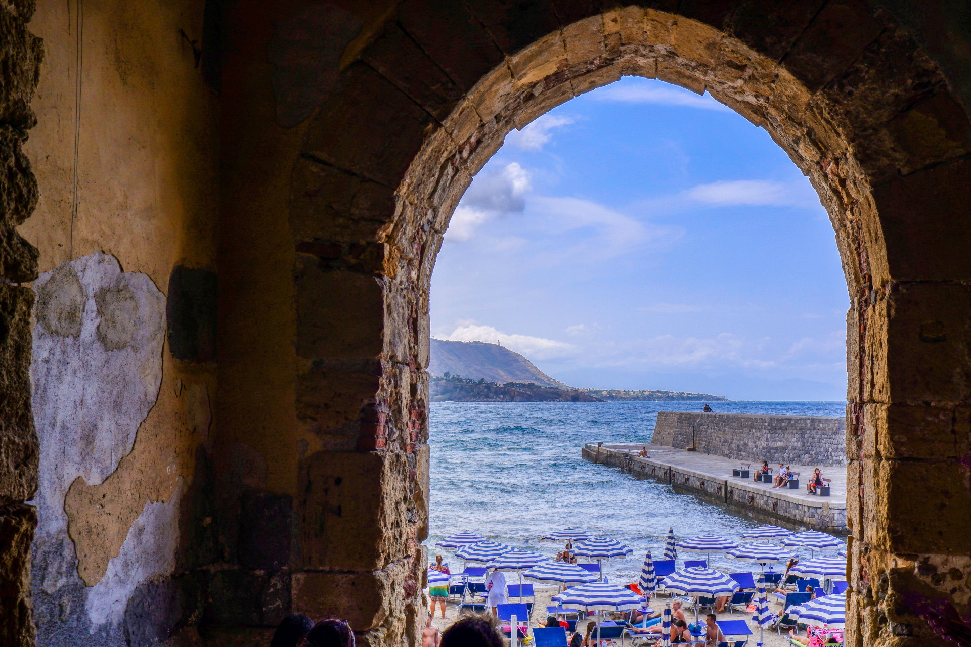 View through old arch at striped beach umbrellas