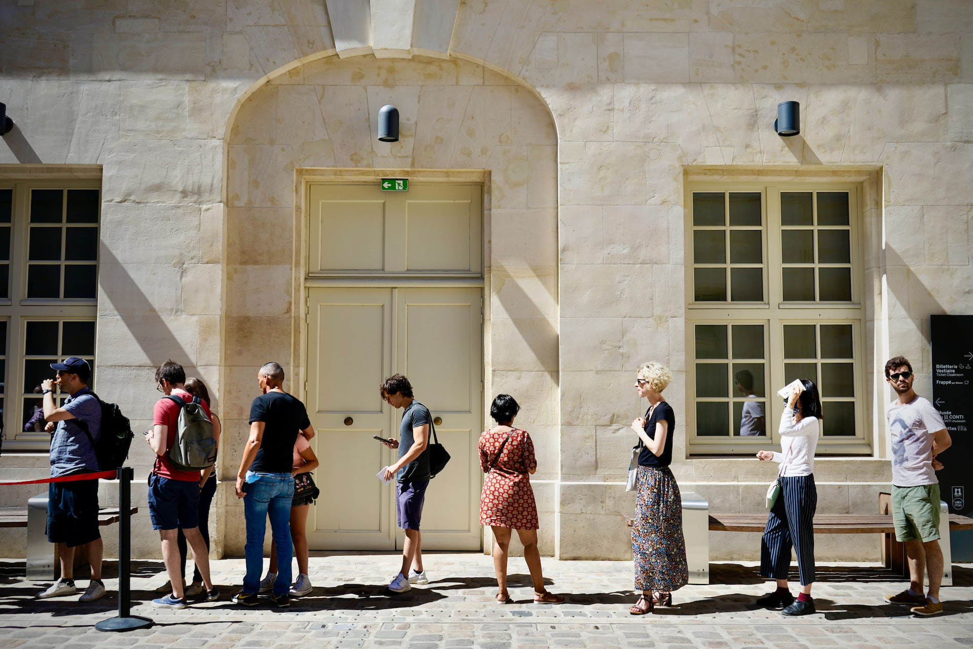 People queuing alongside a tall light-stone building